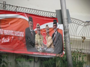 Not a bare head to be seen!  Presidential campaign banner for candidates J. Kalla, current vice-president, and Wiranto, Kalla's vice-presidental choice, with their respective wives shows all wearing head-gear, the women head scarves and the men mosque-hats.